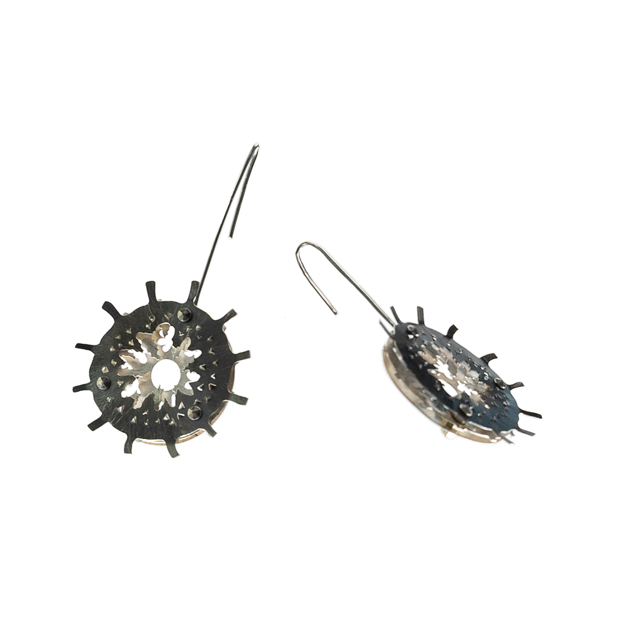 A pair of earrings which consist of 3 layers each. The top layer is laser cut and hand formed and then patinated to create contrast between it and the lower 2 layers. All 3 layers are different designs. The niobium ear wires are angled towards each other in the photo.